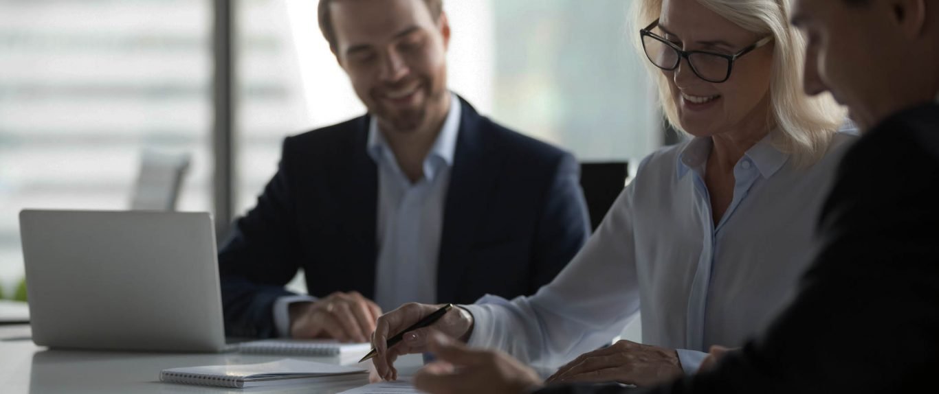 Smiling middle aged businesswoman signing paper contract at group meeting